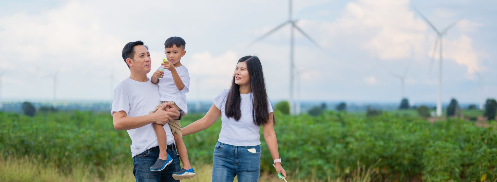 family of four is walking through a field with wind turbines in the background